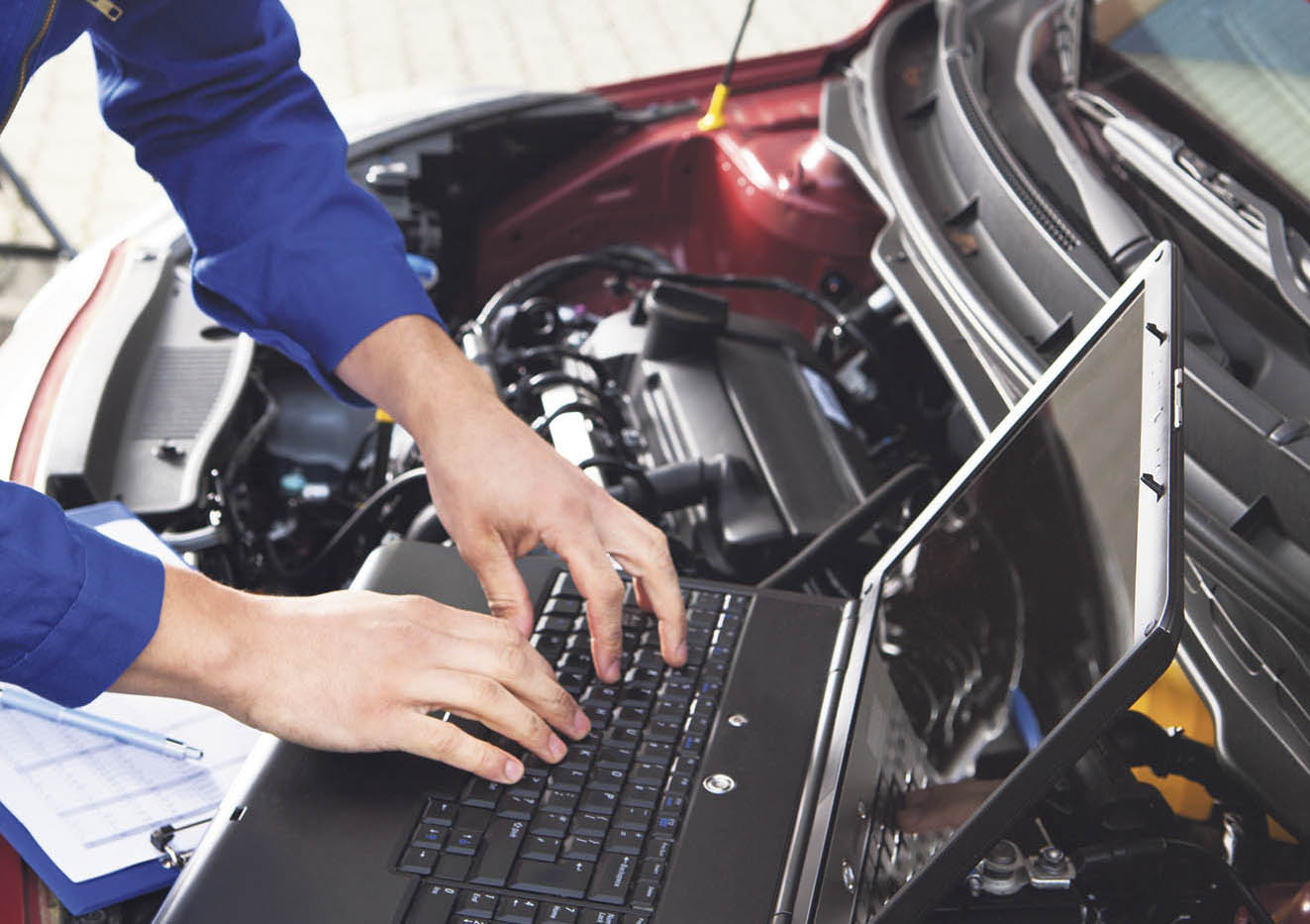 Automechaniker mit Laptop an geöffneter Motorhaube. Thema: KI in der Automobilindustrie